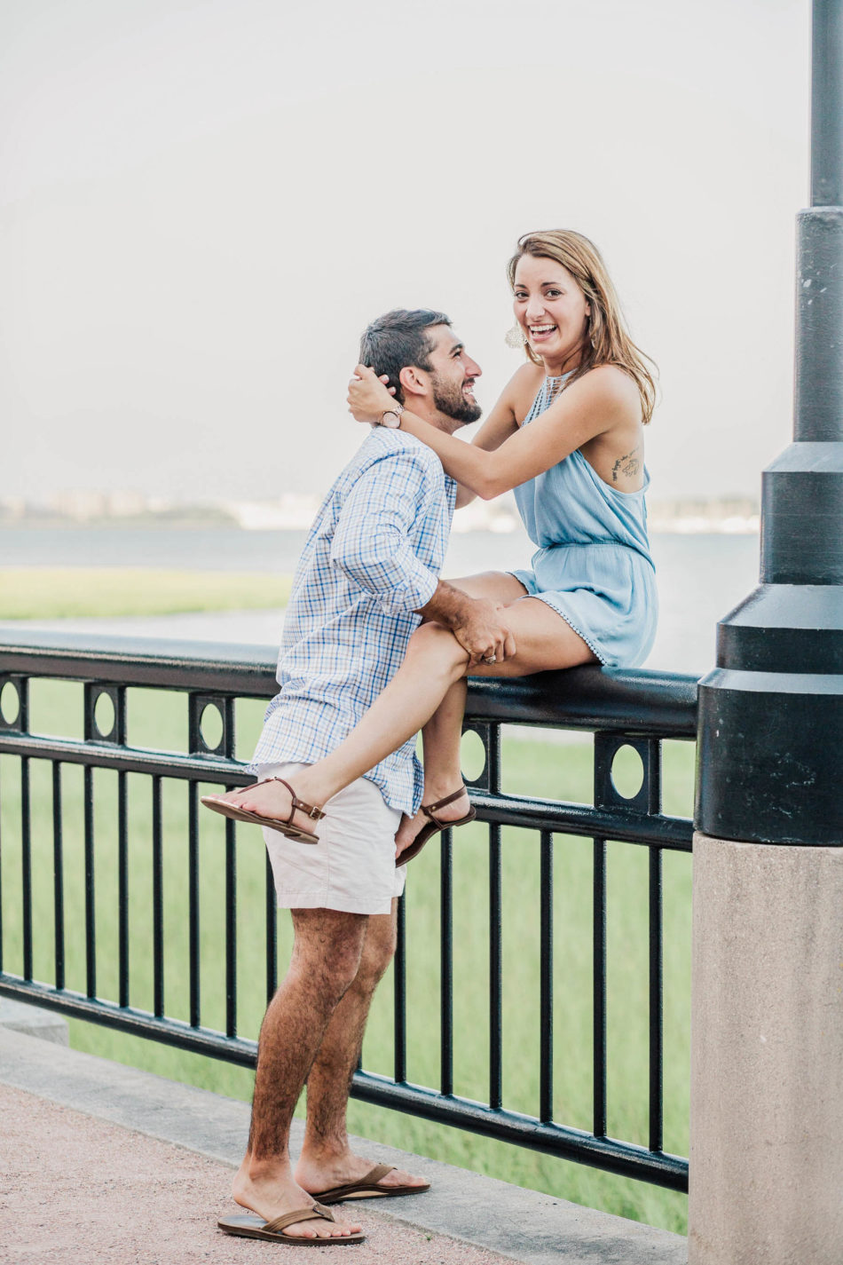 Engaged couple sit on railing with ocean behind them, Waterfront Park, Charleston, South Carolina Kate Timbers Photography. http://katetimbers.com #katetimbersphotography // Charleston Photography // Inspiration