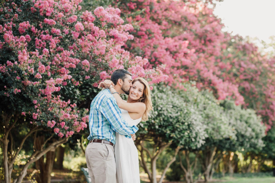 Engaged couple cuddle on path near blooming pink trees, Hampton Park, Charleston, South Carolina Kate Timbers Photography. http://katetimbers.com #katetimbersphotography // Charleston Photography // Inspiration