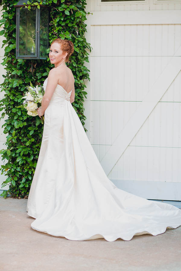 Bride poses with train by white barn doors and ivy wall on her Charleston wedding at Old Wide Awake Plantation. Kate Timbers Photography. katetimbers.com